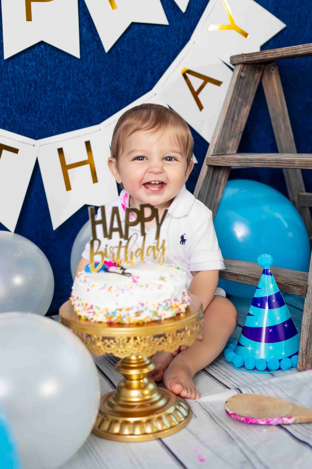Birthday celebration with decorated cake on gold stand, blue balloons, and party decorations.