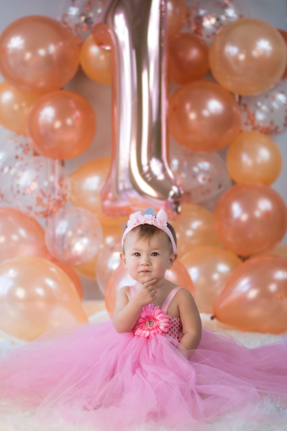 Pink and peach balloon backdrop with tulle decorations for first birthday celebration.
