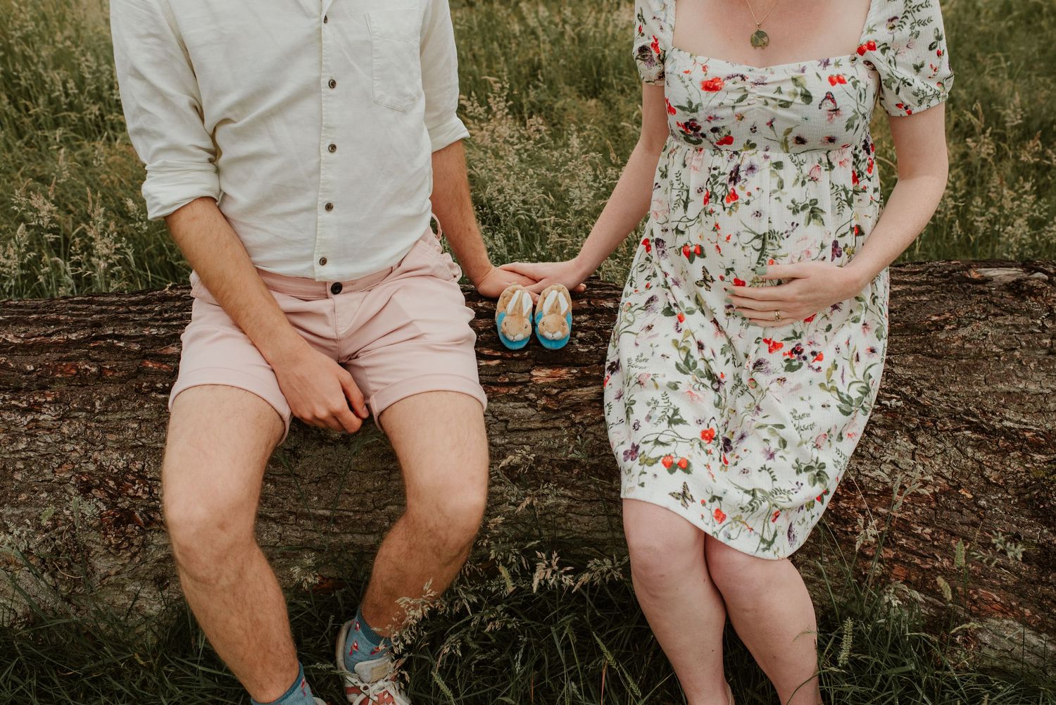 Couple sitting on log holding ultrasound photos in casual summer attire.