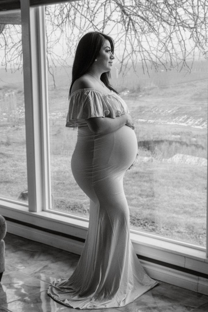 Maternity photoshoot by large windows in black and white tones.
