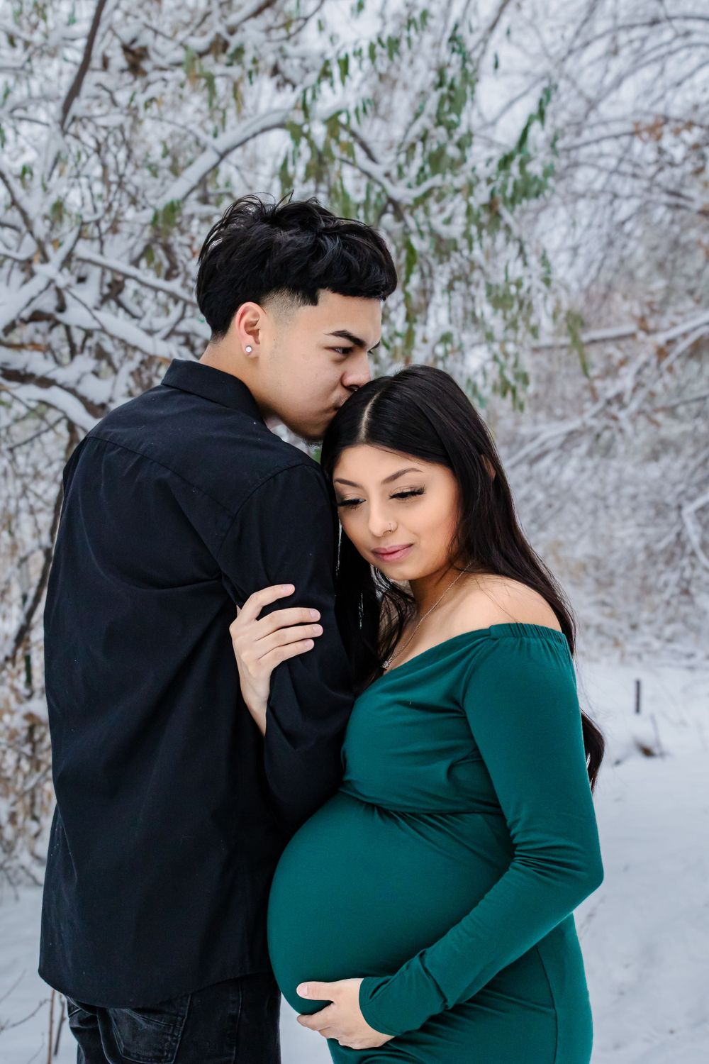 Romantic winter photoshoot featuring a couple embracing in the snow against bare trees.