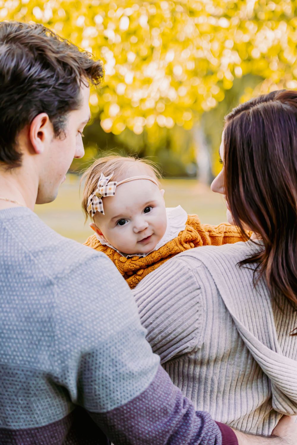 Family portrait in autumn setting with golden leaves in background.