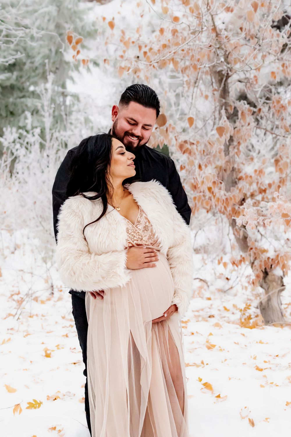 A romantic winter photoshoot with a couple embracing in a snowy forest setting.