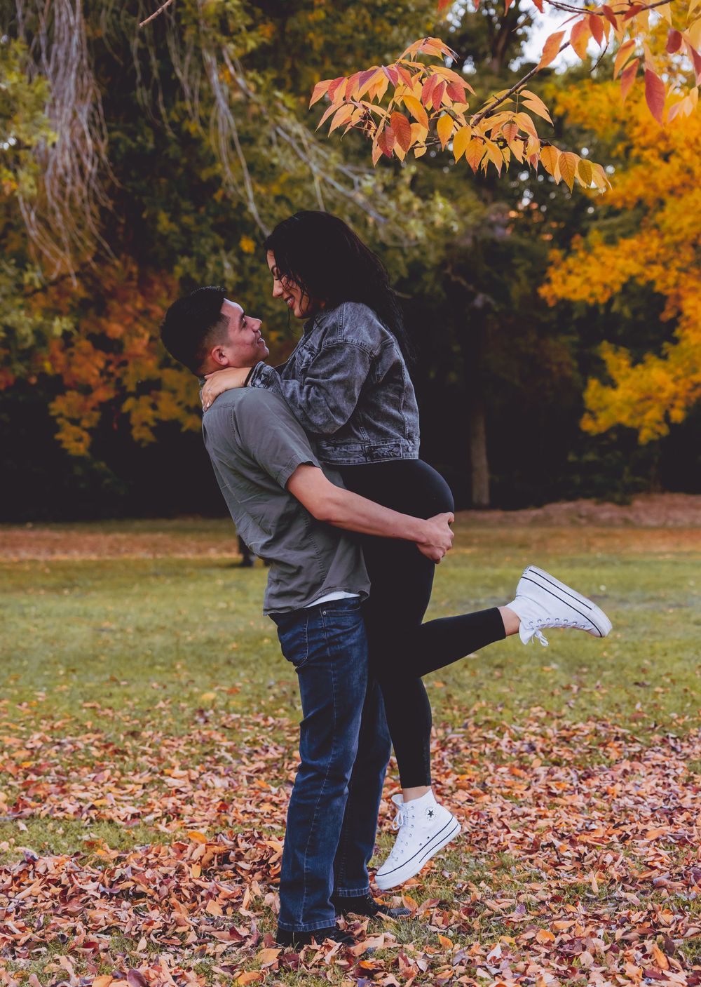 Couple sharing tender moments in a park filled with vibrant autumn foliage.