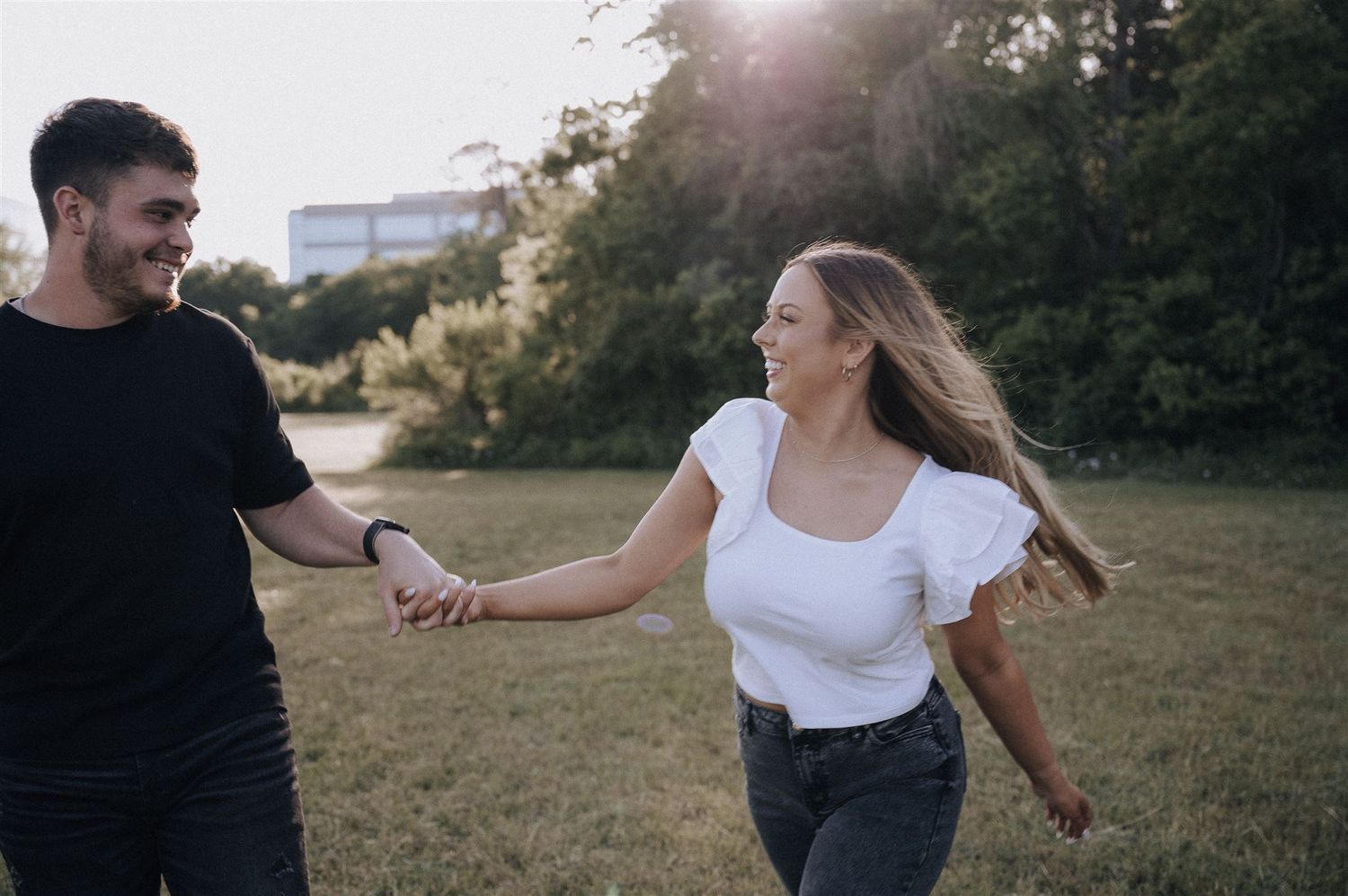 Playful couple holding hands while running through a sunny field.