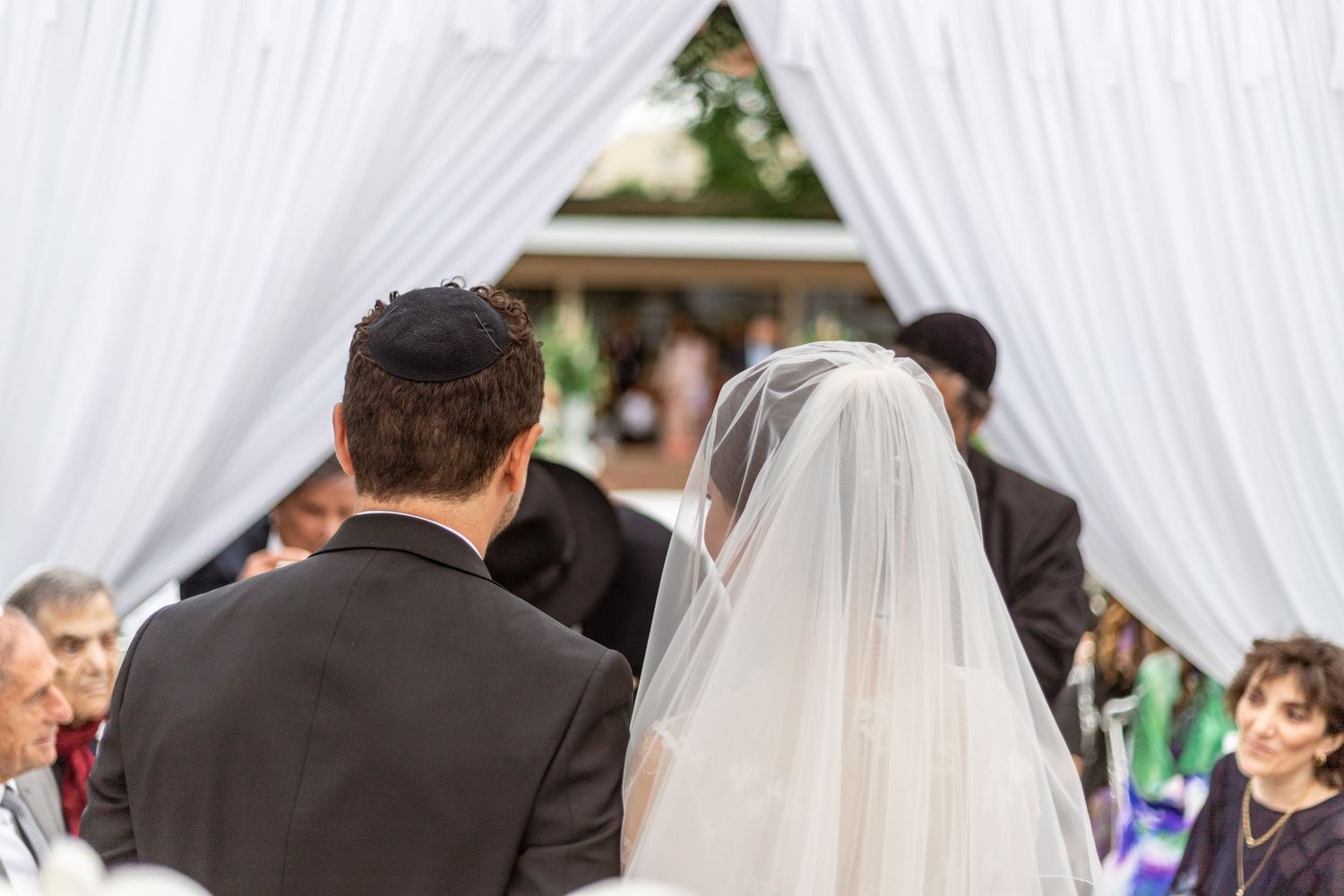 A wedding ceremony view through white draped fabric showing the couple at the altar.