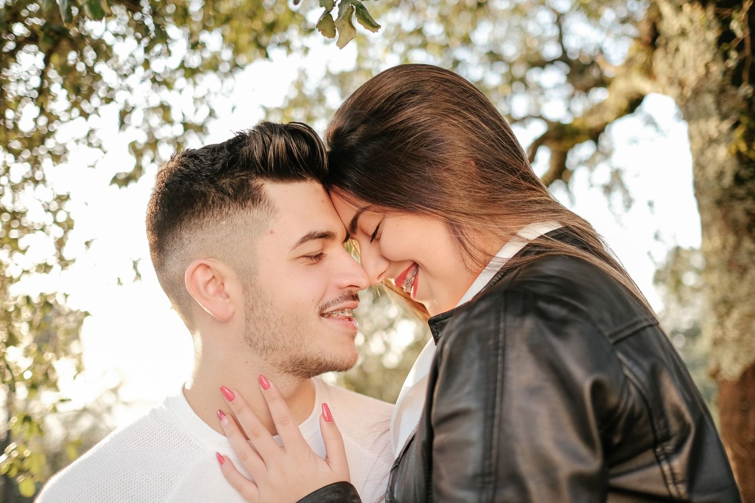 Intimate couple sharing a tender moment outdoors with sunlit trees in the background.