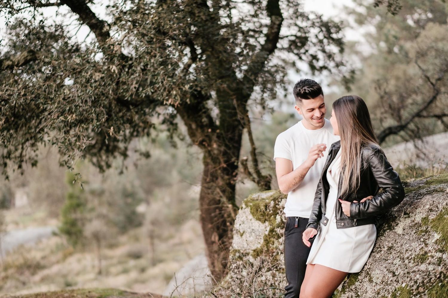 Couple sharing intimate moment on rocky hillside under sprawling tree.