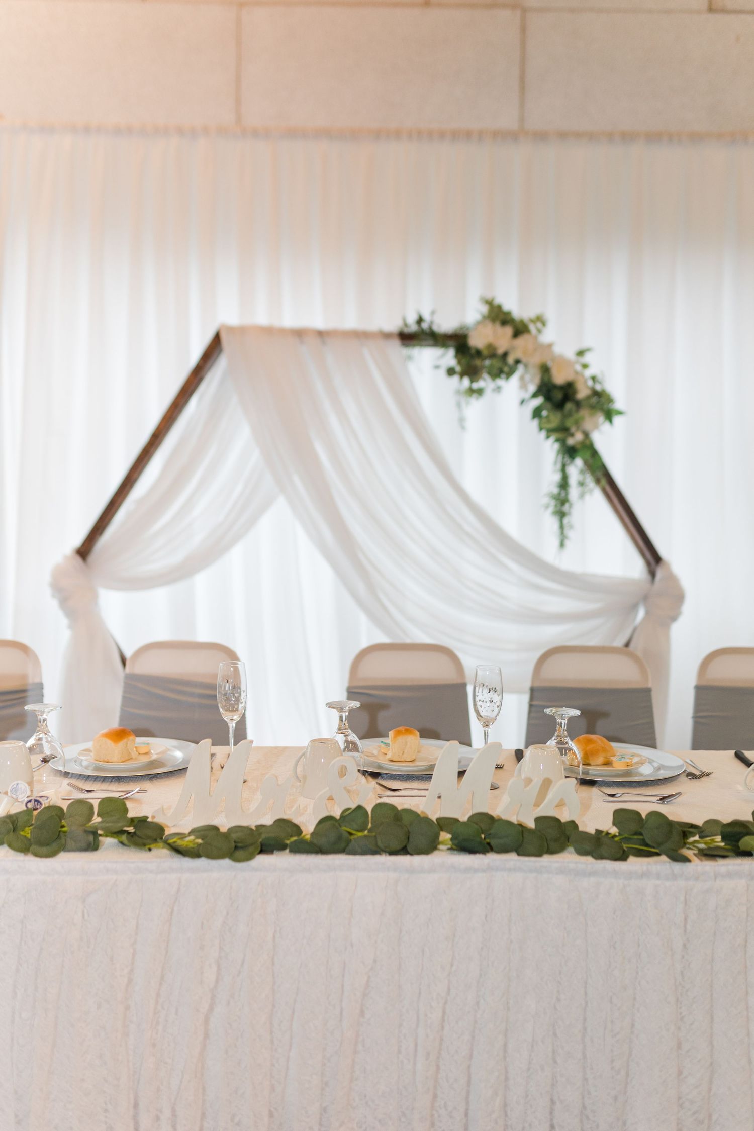 Elegant wedding head table setup with white draping arch and floral decorations.
