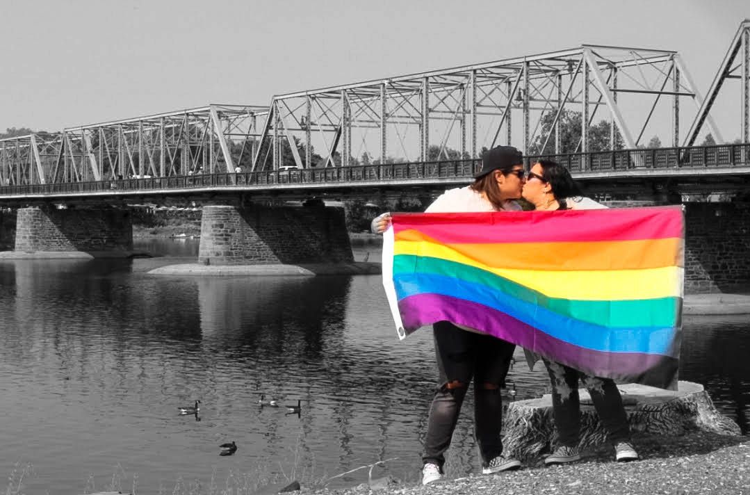 Selective color photo showing a pride flag against black and white bridge background.