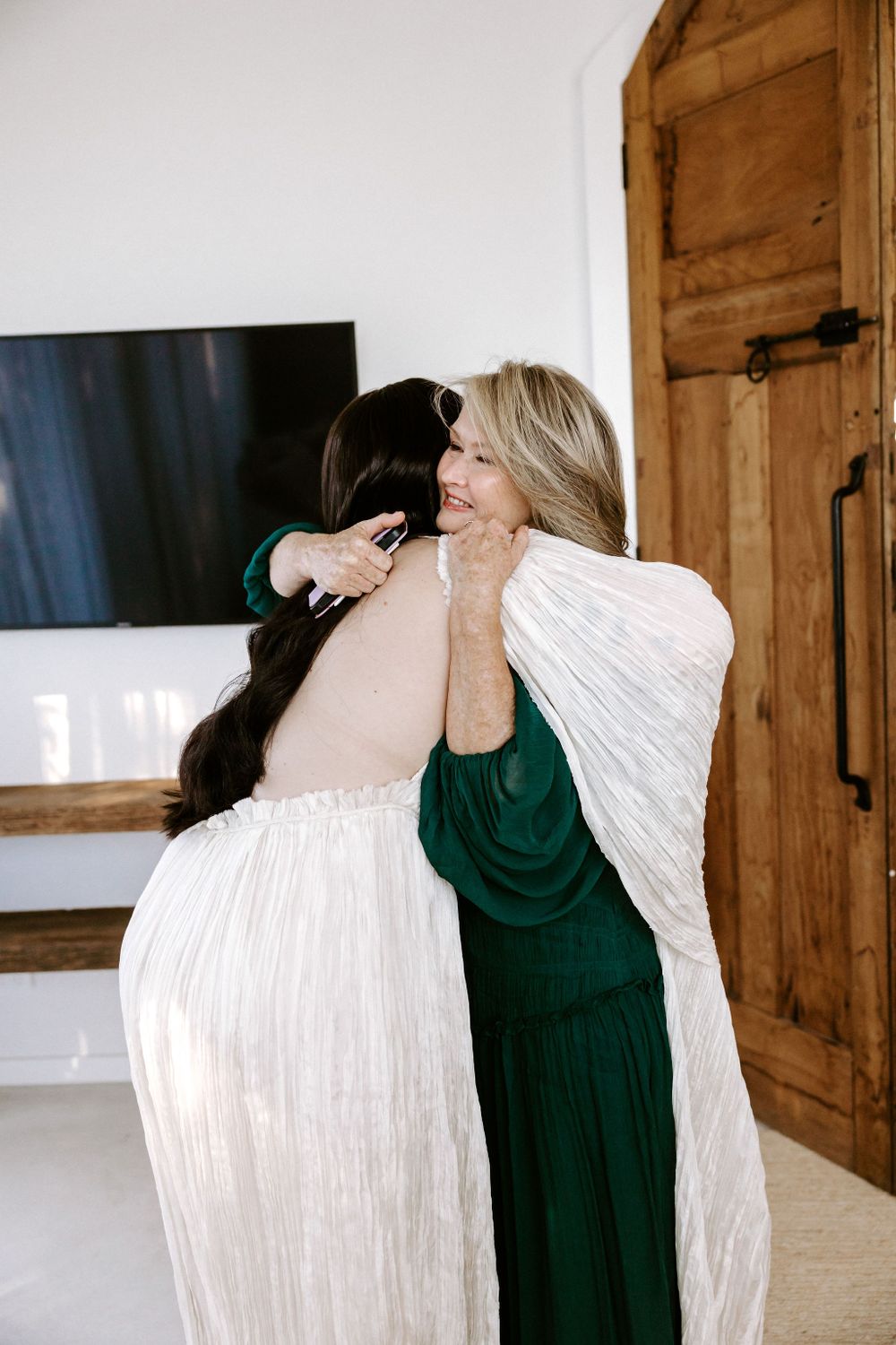 An emotional embrace shared between two people in white and emerald dresses.