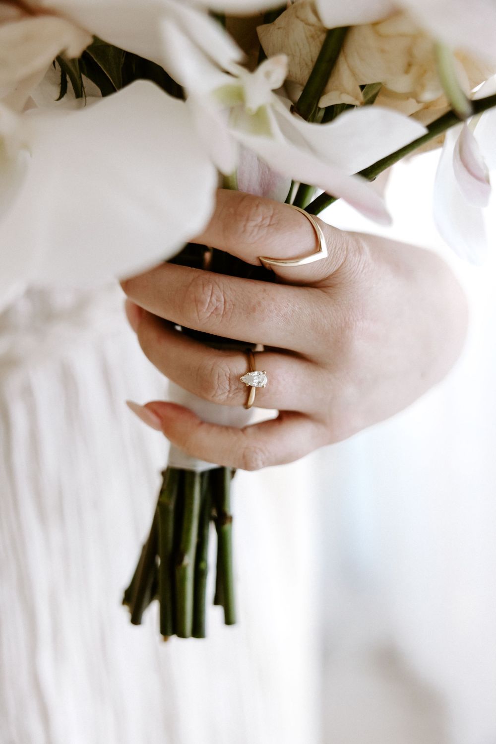 Close up of hands holding white flowers with an engagement ring.