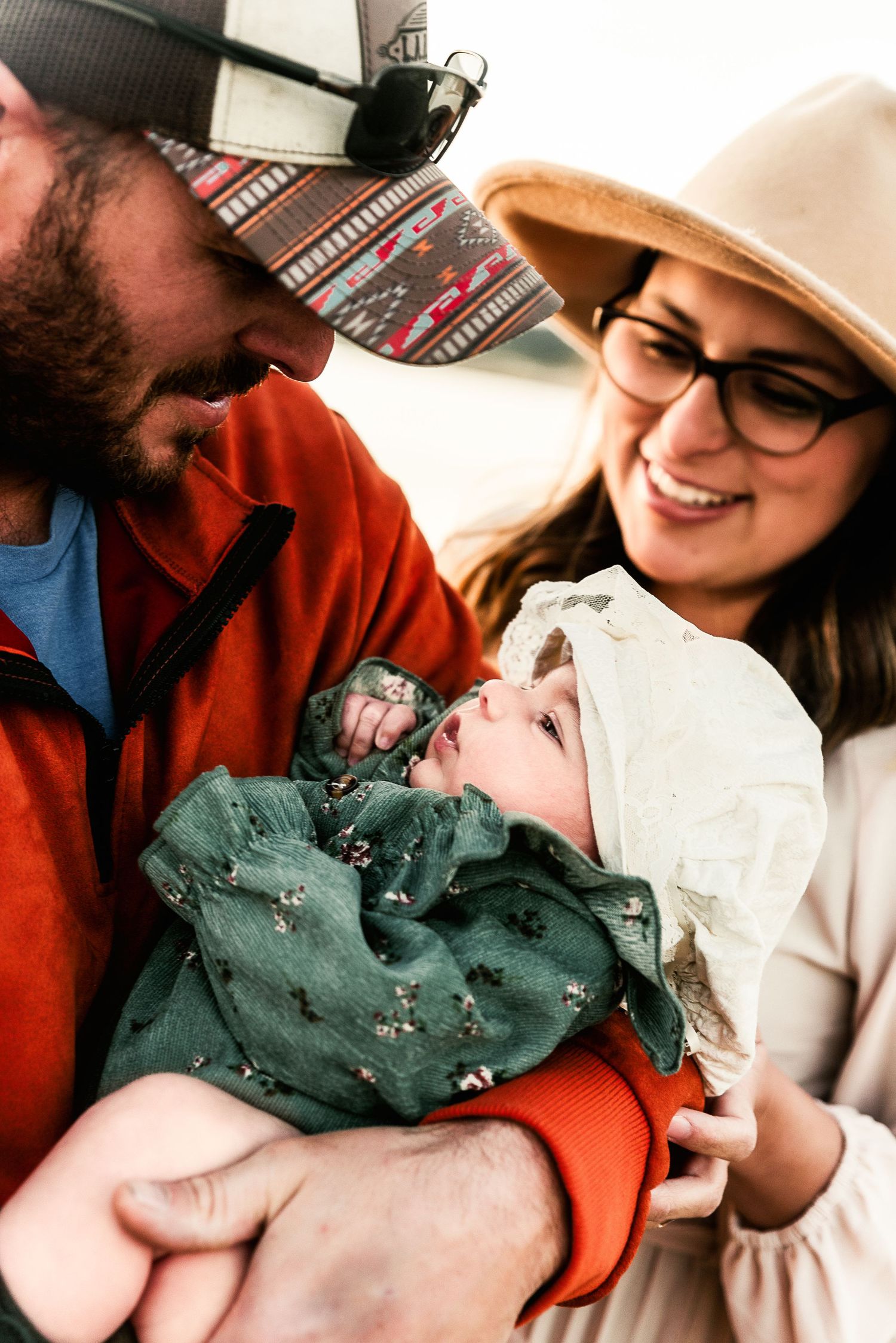 A mother and father stare lovingly at their daughter in a bonnet.