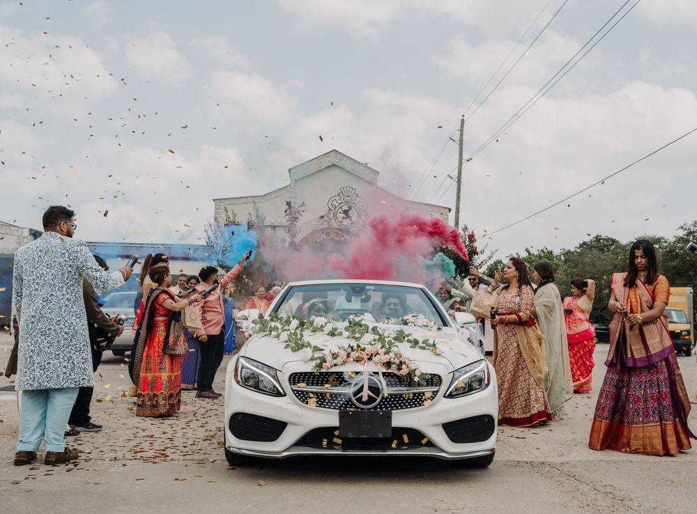 Colorful smoke bombs and confetti fill the air around a decorated white car during a wedding celebration.
