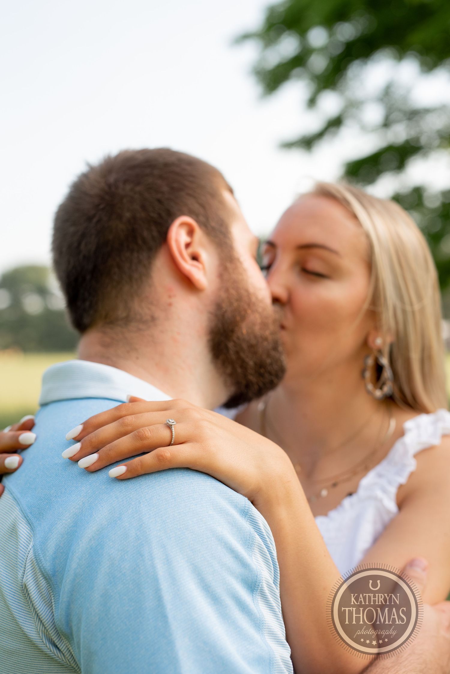 An intimate moment captured between a couple sharing a kiss in a grassy outdoor setting.