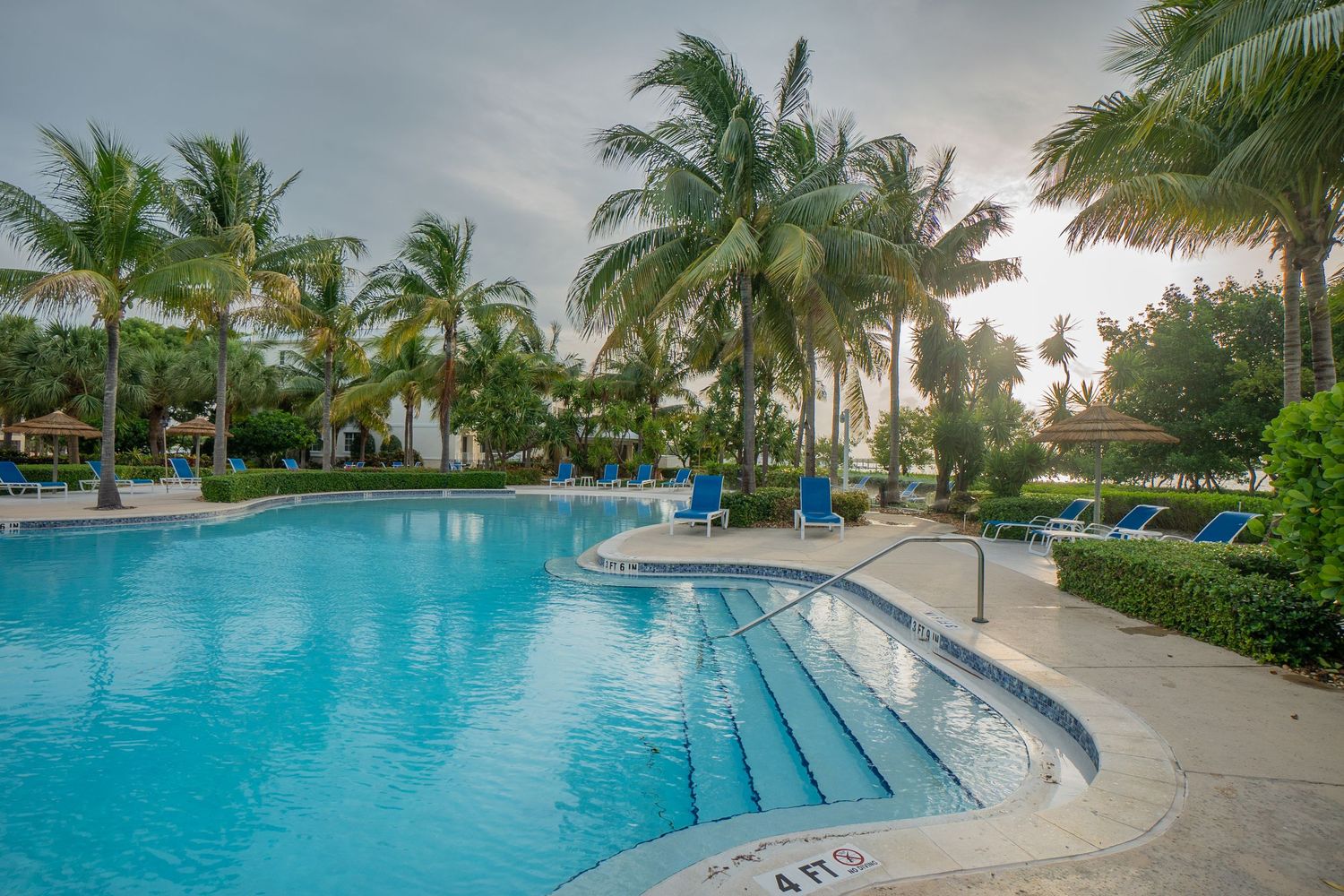 Panoramic view of a luxury resort pool surrounded by palm trees at sunset.