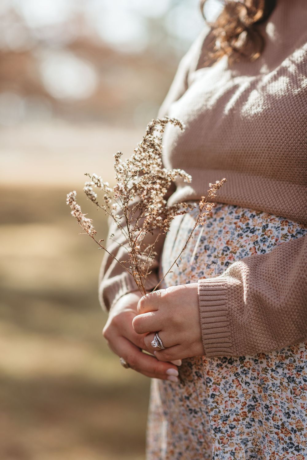 Close-up of hands holding dried flowers against a floral dress and beige sweater.