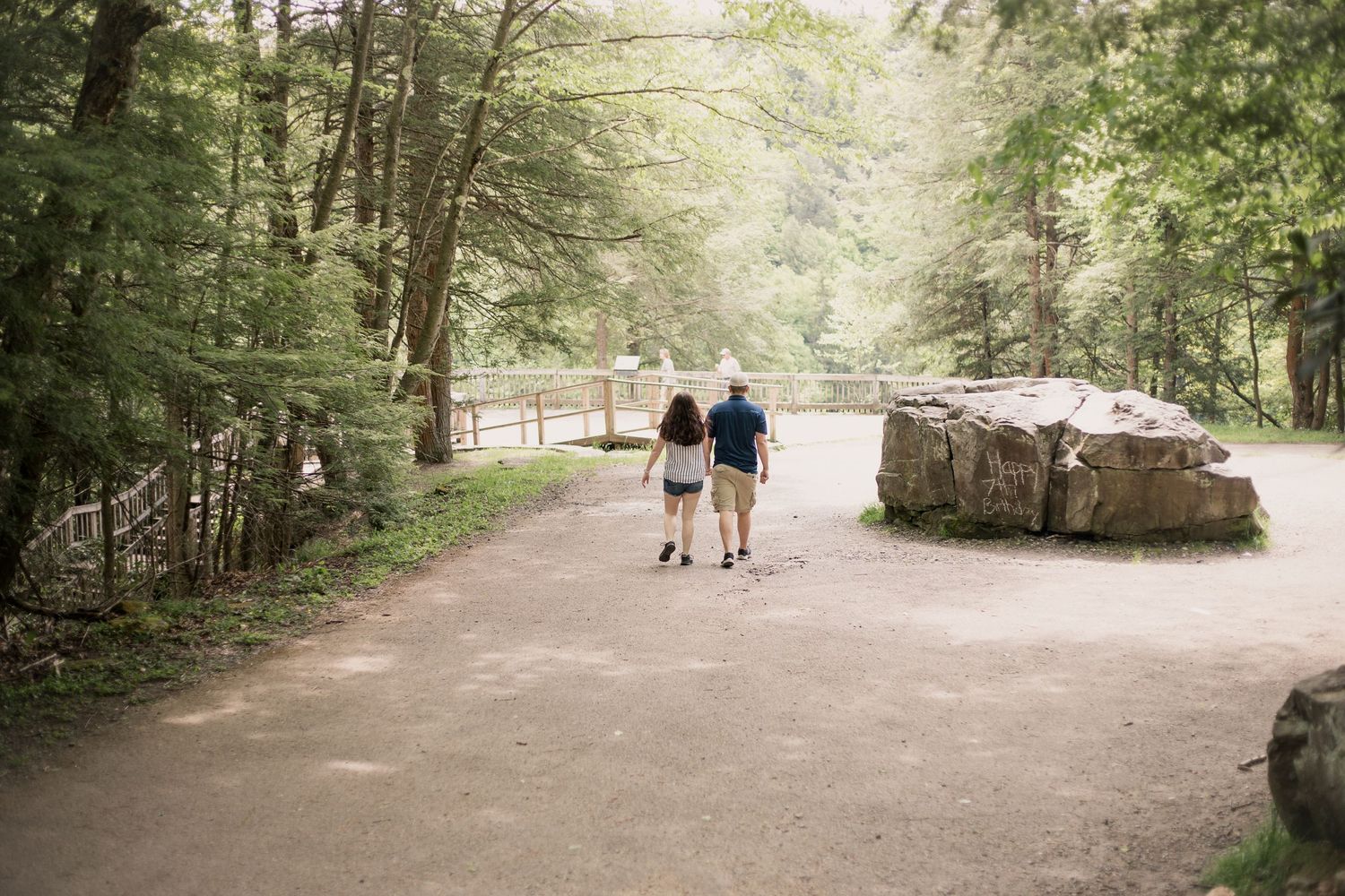 Couple walking along wooded nature trail during summer engagement session.