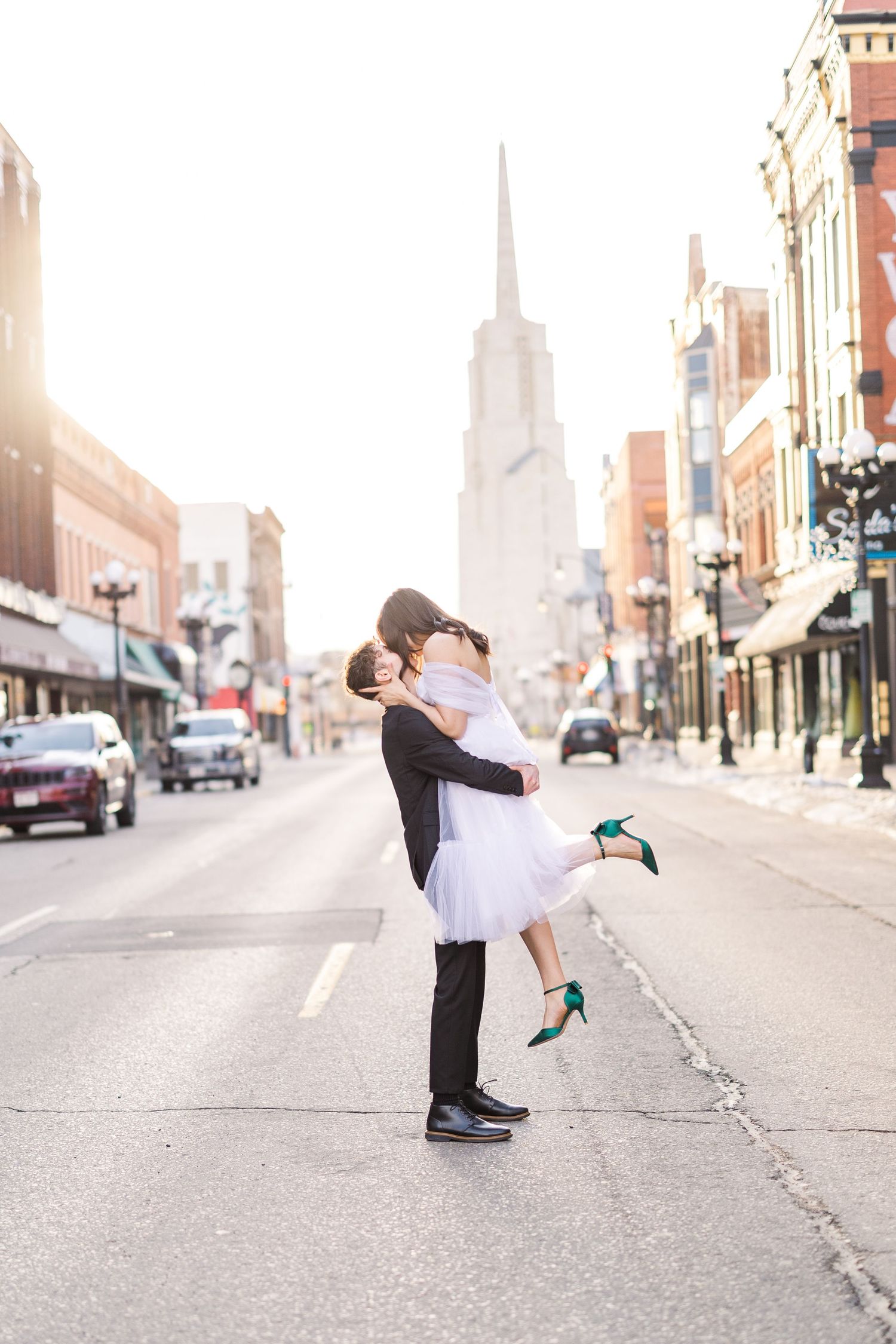 Romantic urban wedding photo with couple embracing in front of sunlit city street.