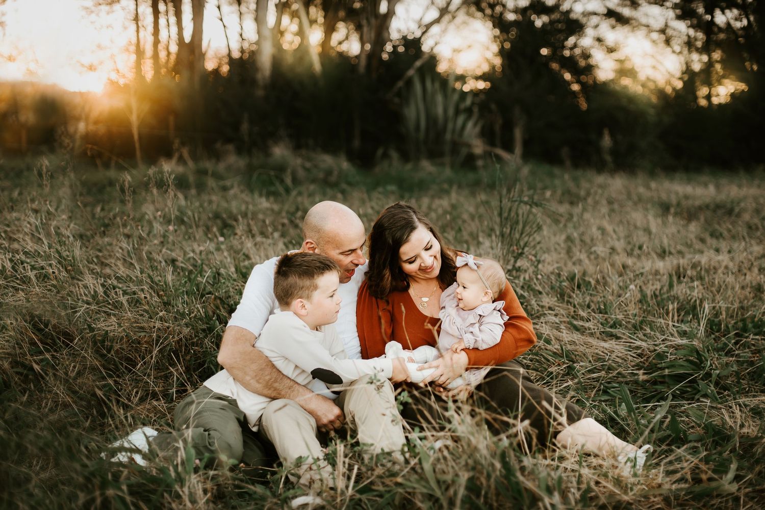 Candid family photo session in grassy field during golden hour sunset.