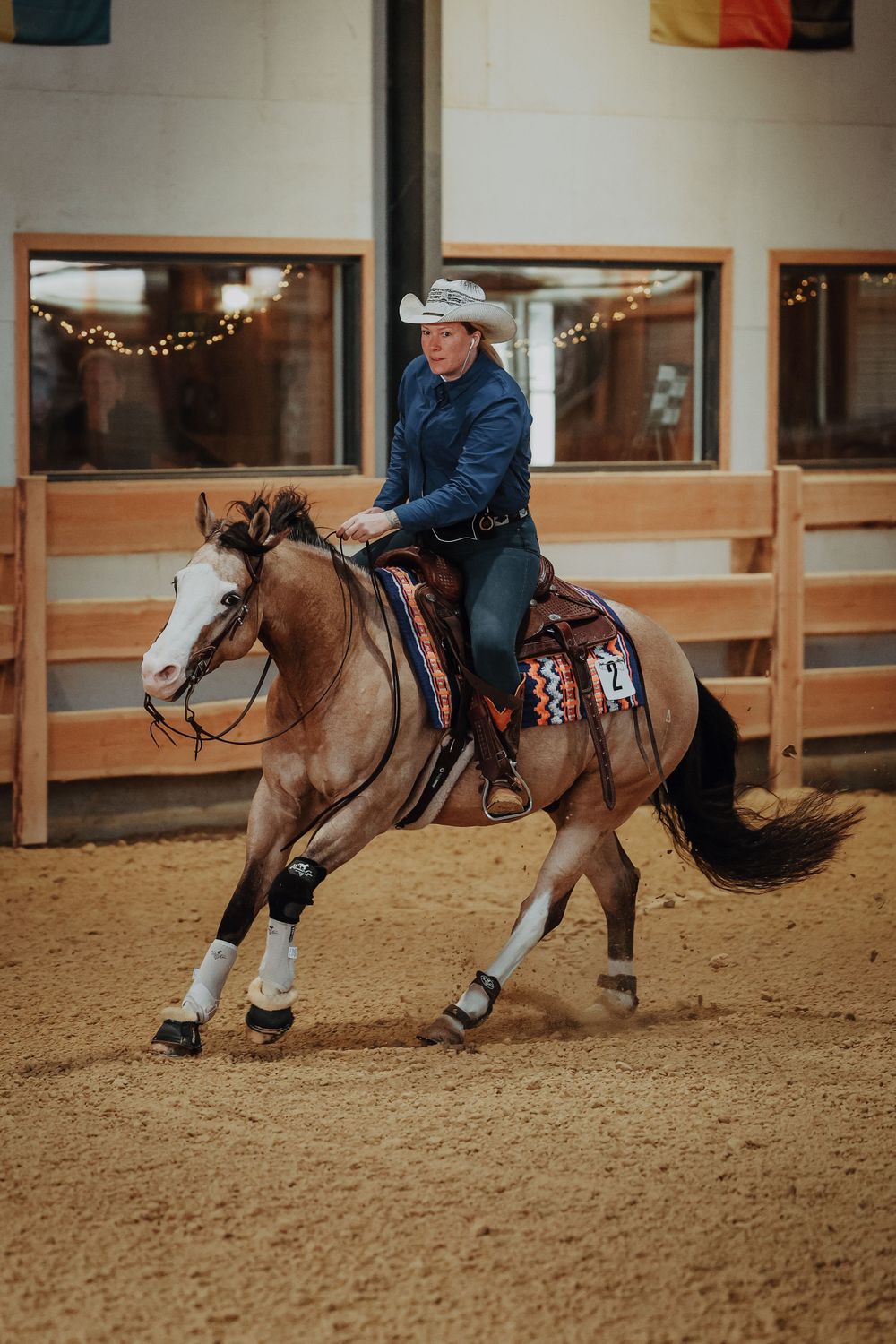 A paint horse and rider perform reining maneuvers in an indoor arena with viewing windows.