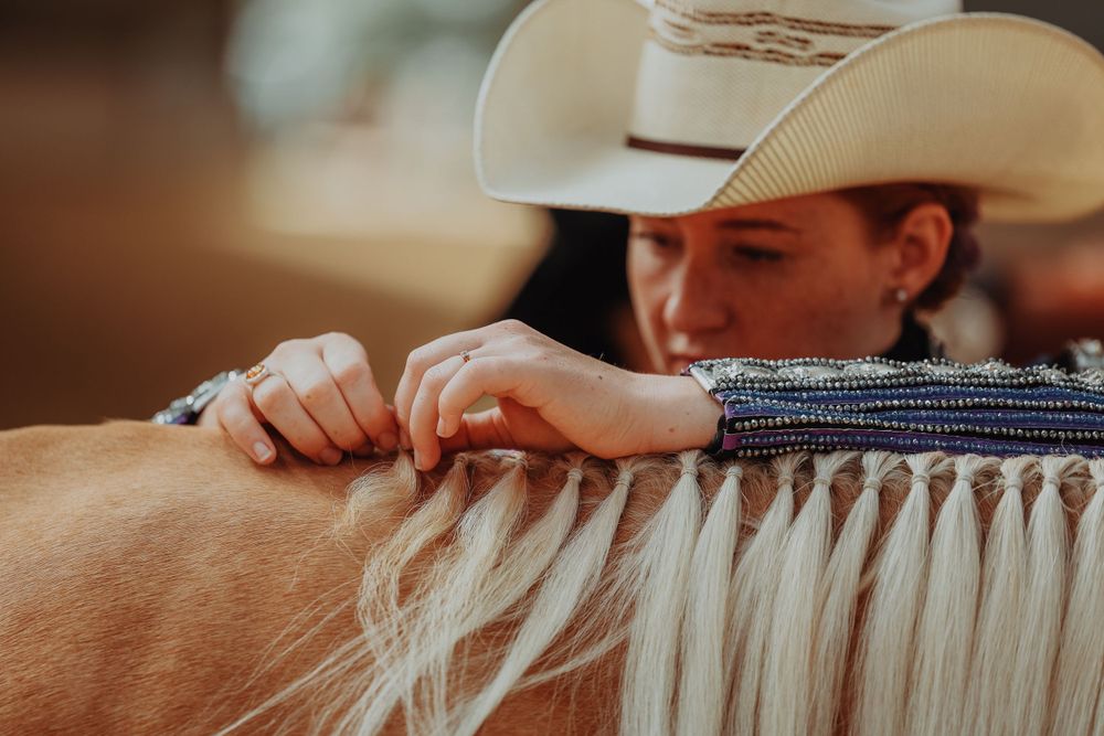 Close-up of hands braiding a horse's mane at an equestrian event.