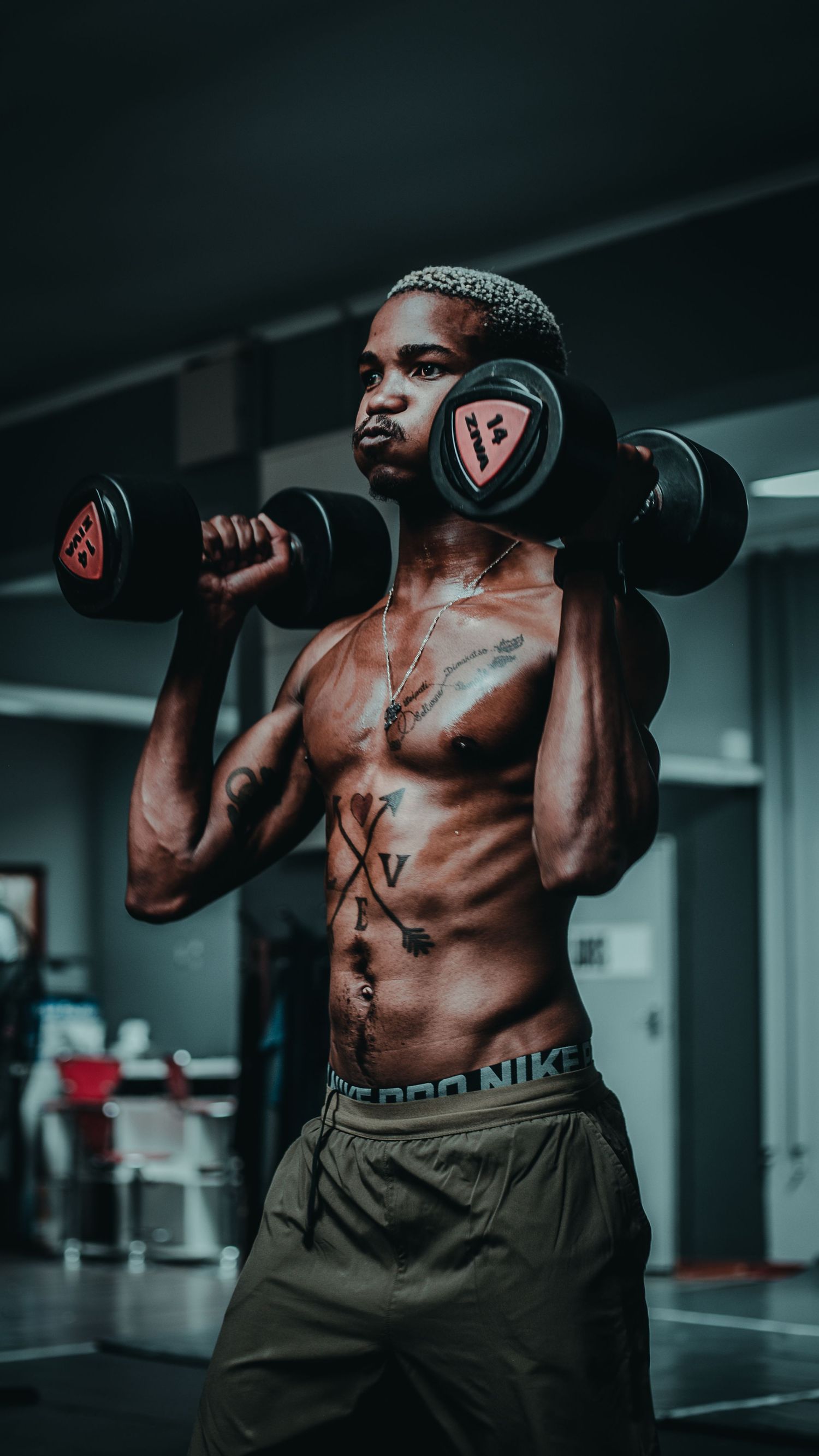 Athletic person exercising with dumbbells in gym wearing headphones.