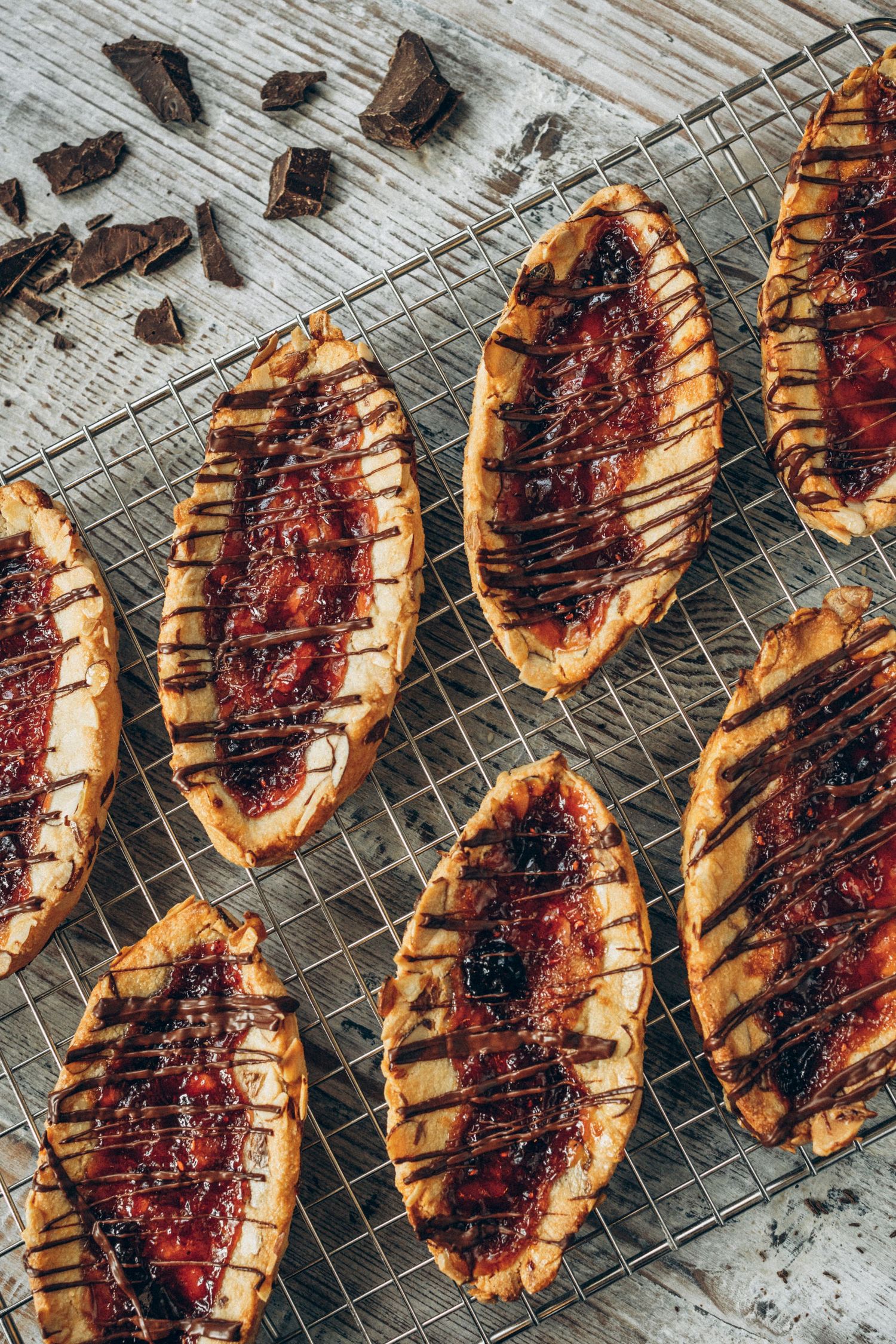 Rustic pastries with dark fruit filling cooling on a wire rack with chocolate pieces.