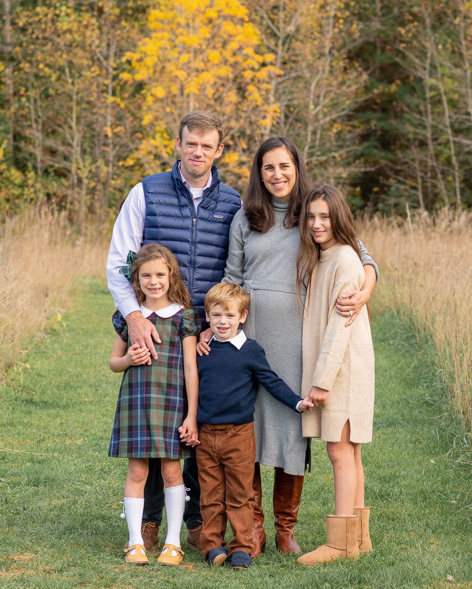 Family portrait outdoors with colorful fall foliage in the background.