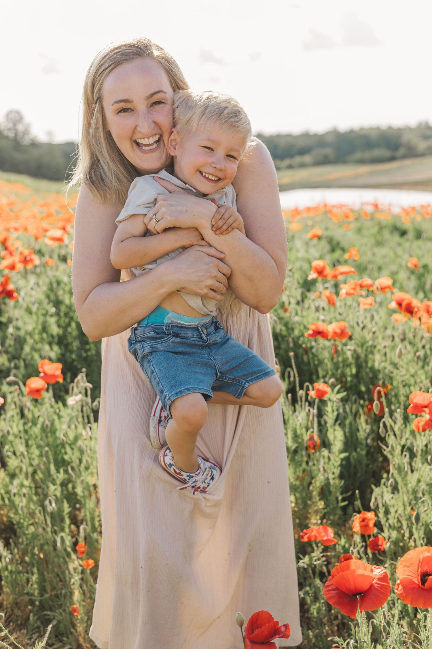 Happy mother holding her laughing toddler son in a vibrant red poppy flower field.