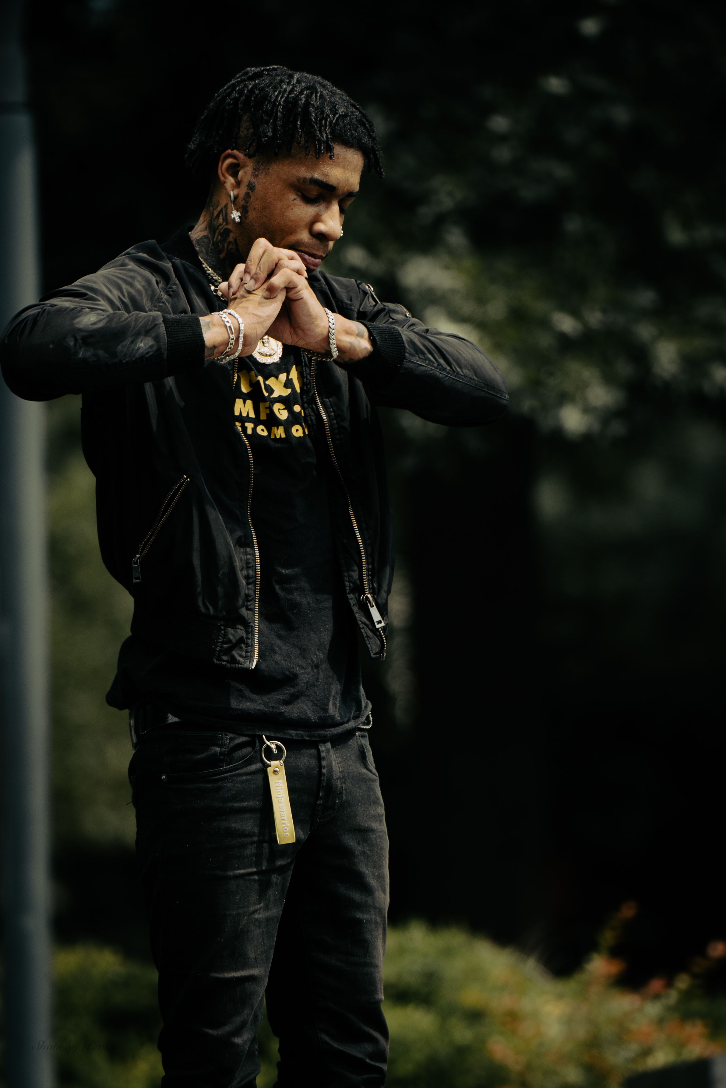 Artistic portrait of someone in dark clothing against a blurred natural background.