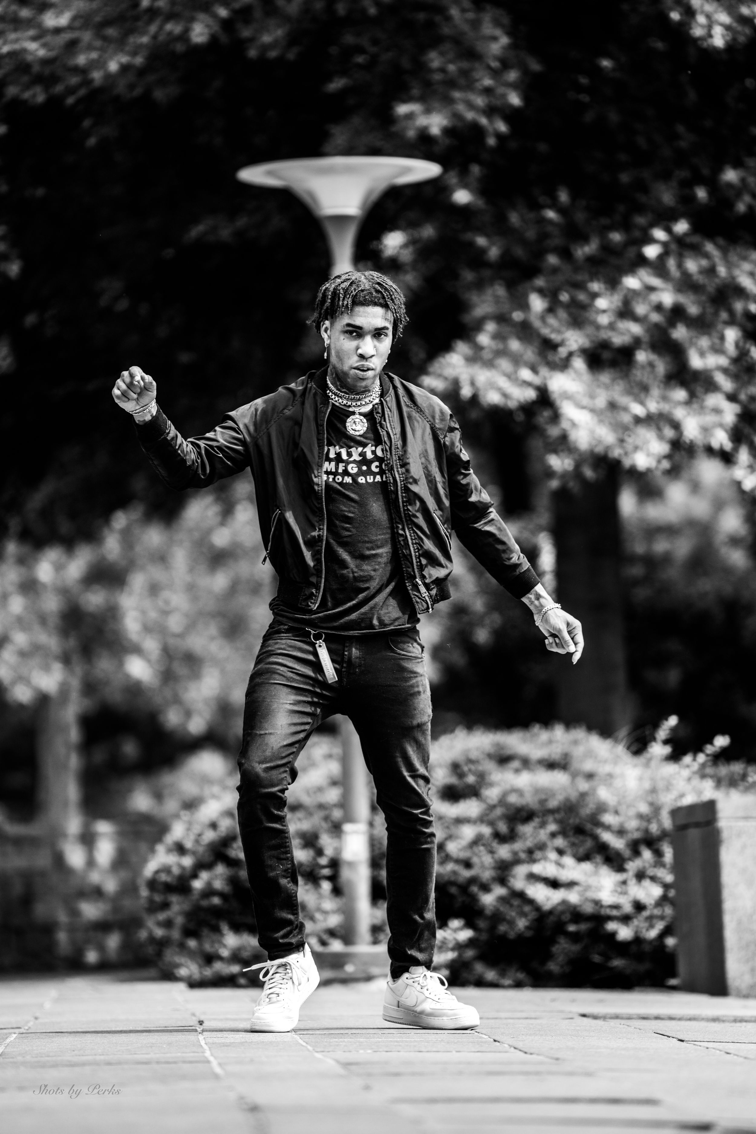 Dynamic street photograph of someone in casual attire striking a pose in black and white.