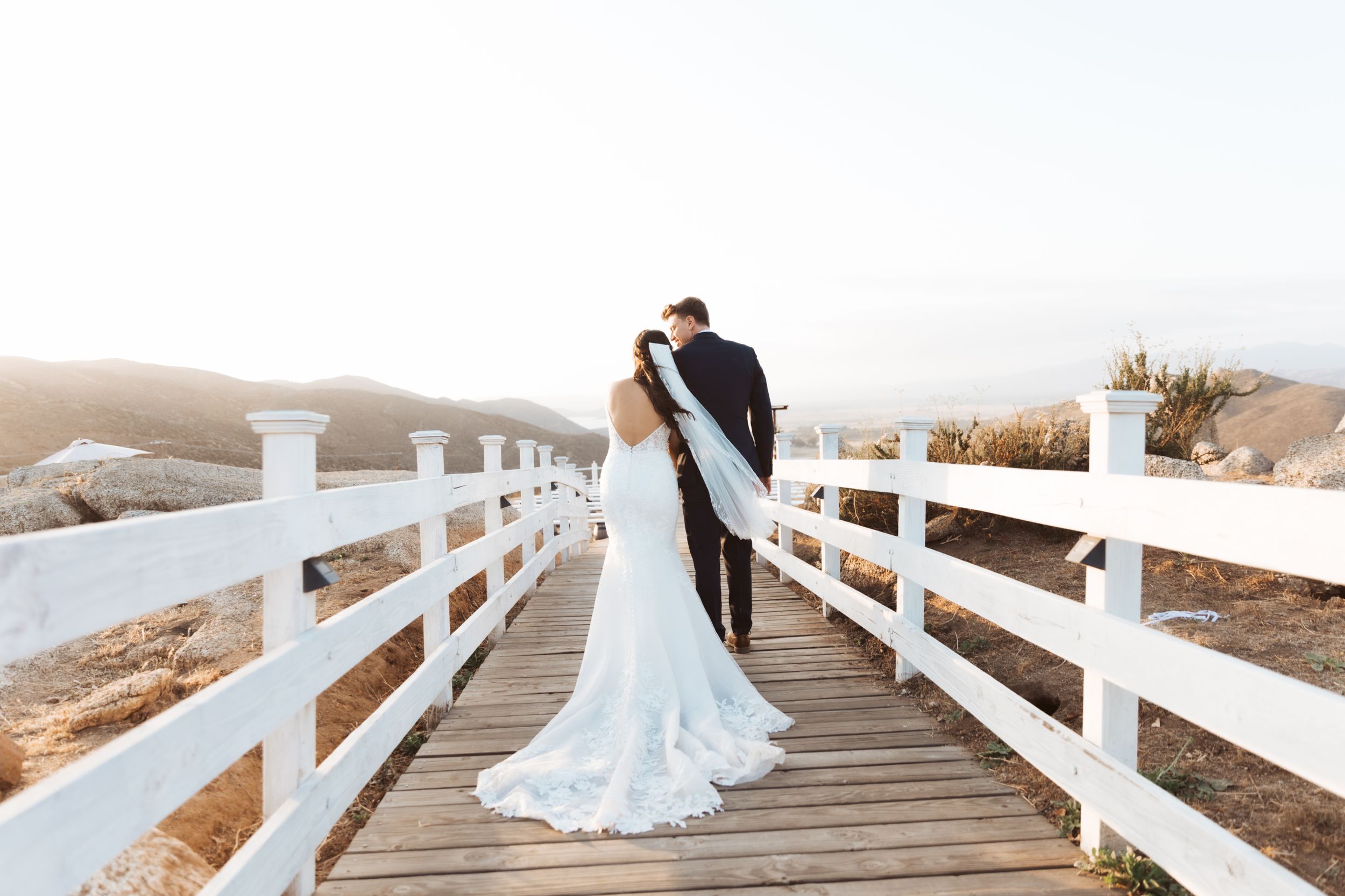 Newlyweds sharing romantic moment on white wooden bridge at sunset.