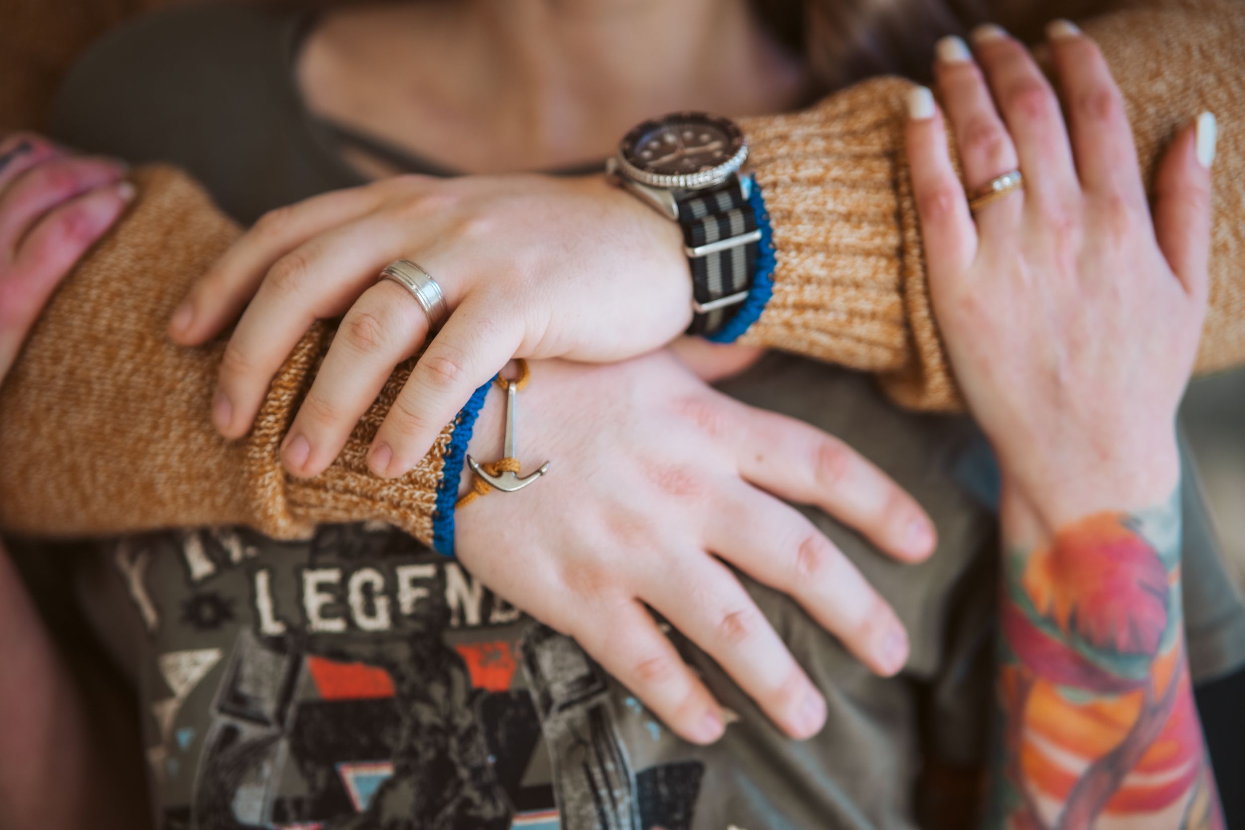 Close-up of hands with tattoos and jewelry embracing in warm sweater sleeves.