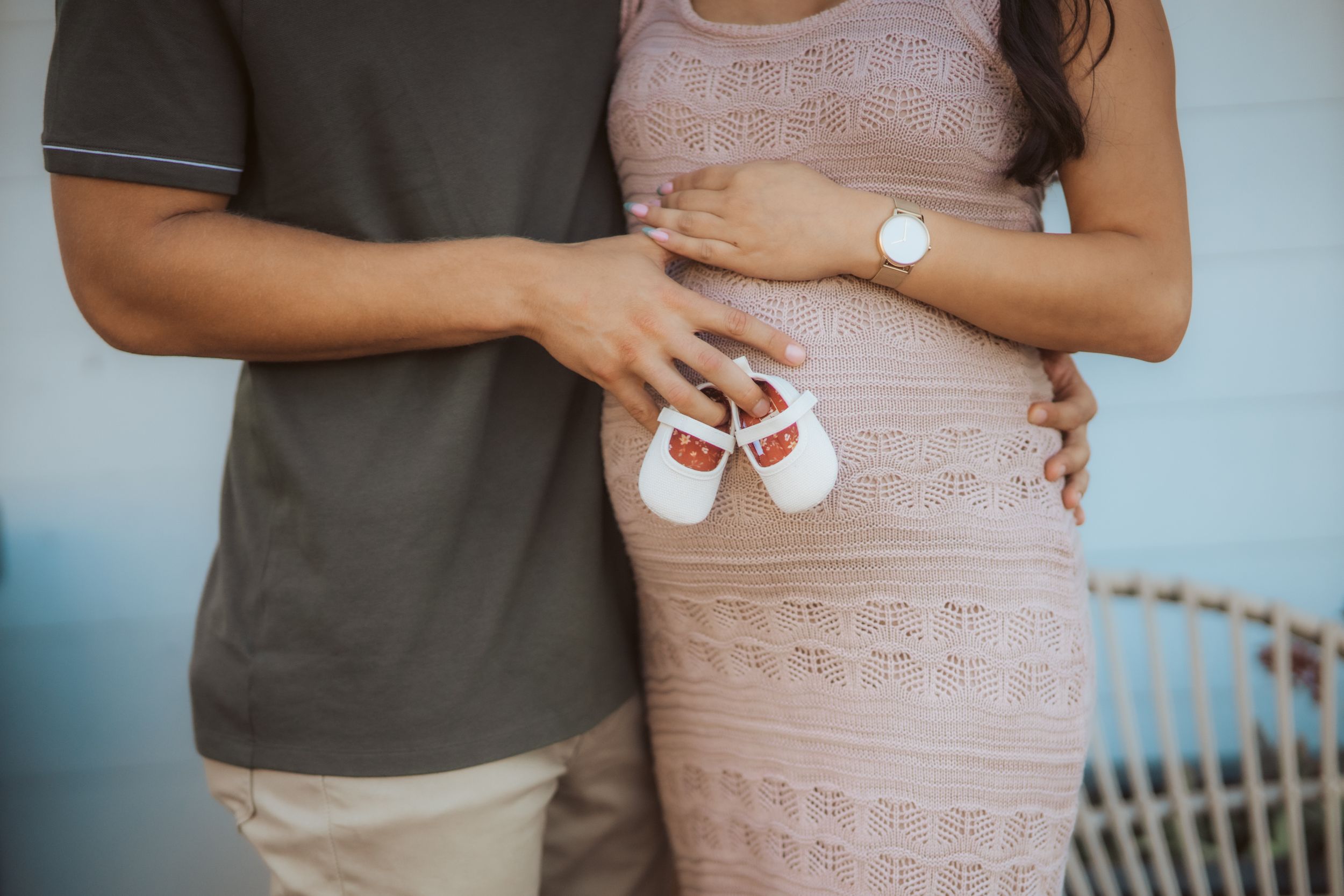 Couple holding infant shoes against a pregnant belly in a tender moment.