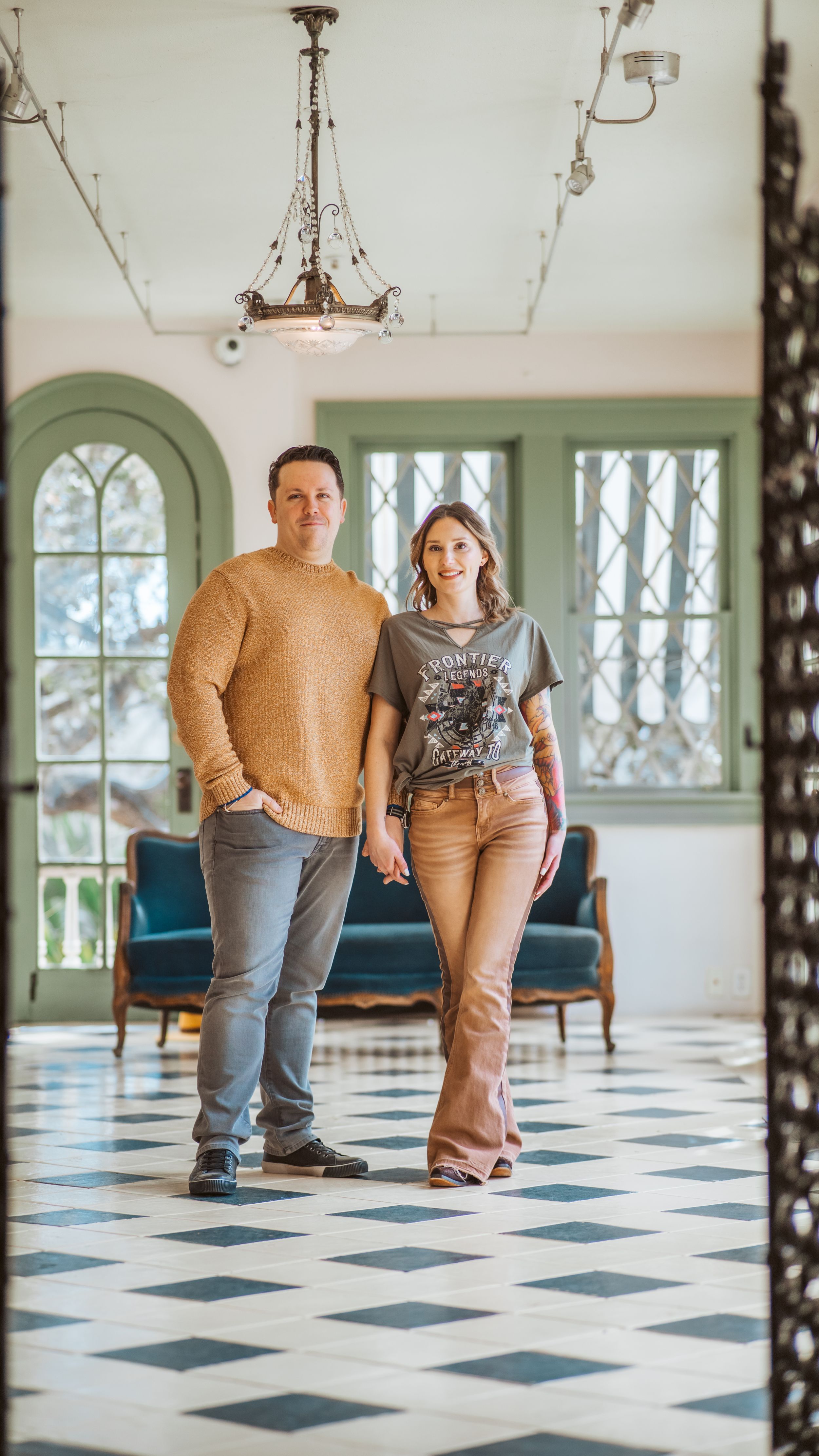 A stylish couple poses in a room with checkered floors and vintage decor.