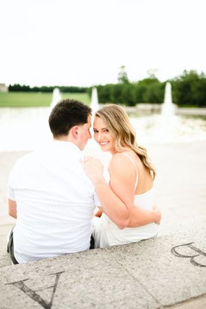 Couple sitting together on stone ledge by water on sunny day.