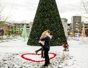 A romantic winter proposal scene with a large Christmas tree and heart shape in snow.