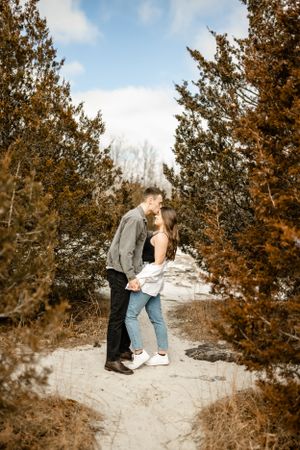 A couple shares an intimate moment on snowy rocks with evergreen trees in the background.