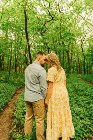 A couple walking hand in hand down a lush green forest trail with dappled sunlight.