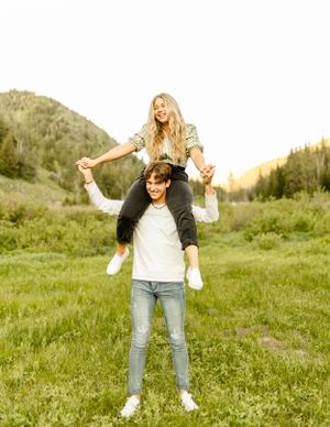 Joyful couple having fun with piggyback rides in a green mountain field.
