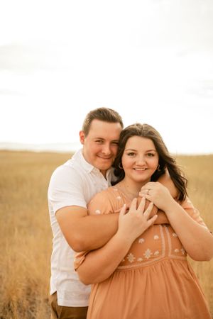 Couple embraces and laughs together in a sunlit field.