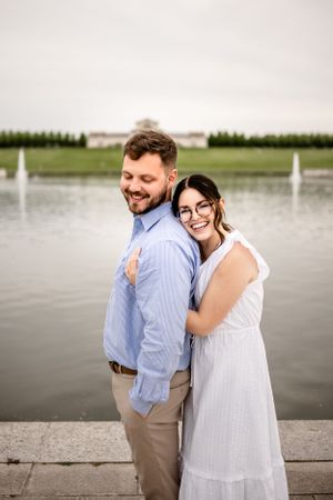 Waterfront engagement session with fountain and landscaped grounds in background.