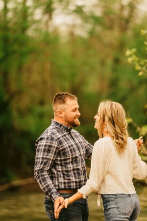 A couple laughing together while sitting outdoors in casual attire with golden sunlight filtering through trees.