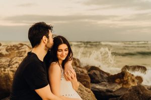 A couple sharing tender moments on a rocky beach with ocean waves in the background.