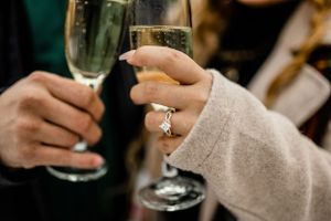 Two champagne glasses being held with an engagement ring visible.