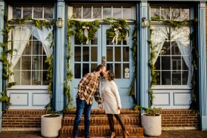 Playful couple photos against blue historic building facade with white trim.