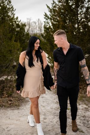 A couple playfully walks together through a winter landscape with pine trees.