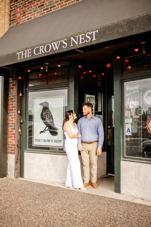 Engagement photos outside The Crow's Nest building with brick facade and storefront signage.