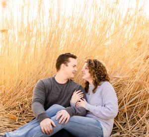 Romantic couple embraces in a golden field of tall grass during sunset.